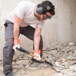 Construction worker collecting construction debris with a shovel. House renovation.